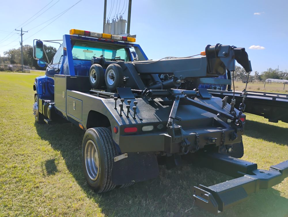 Blue and tan tow truck with crane boom and wrecker equipment parked on grass