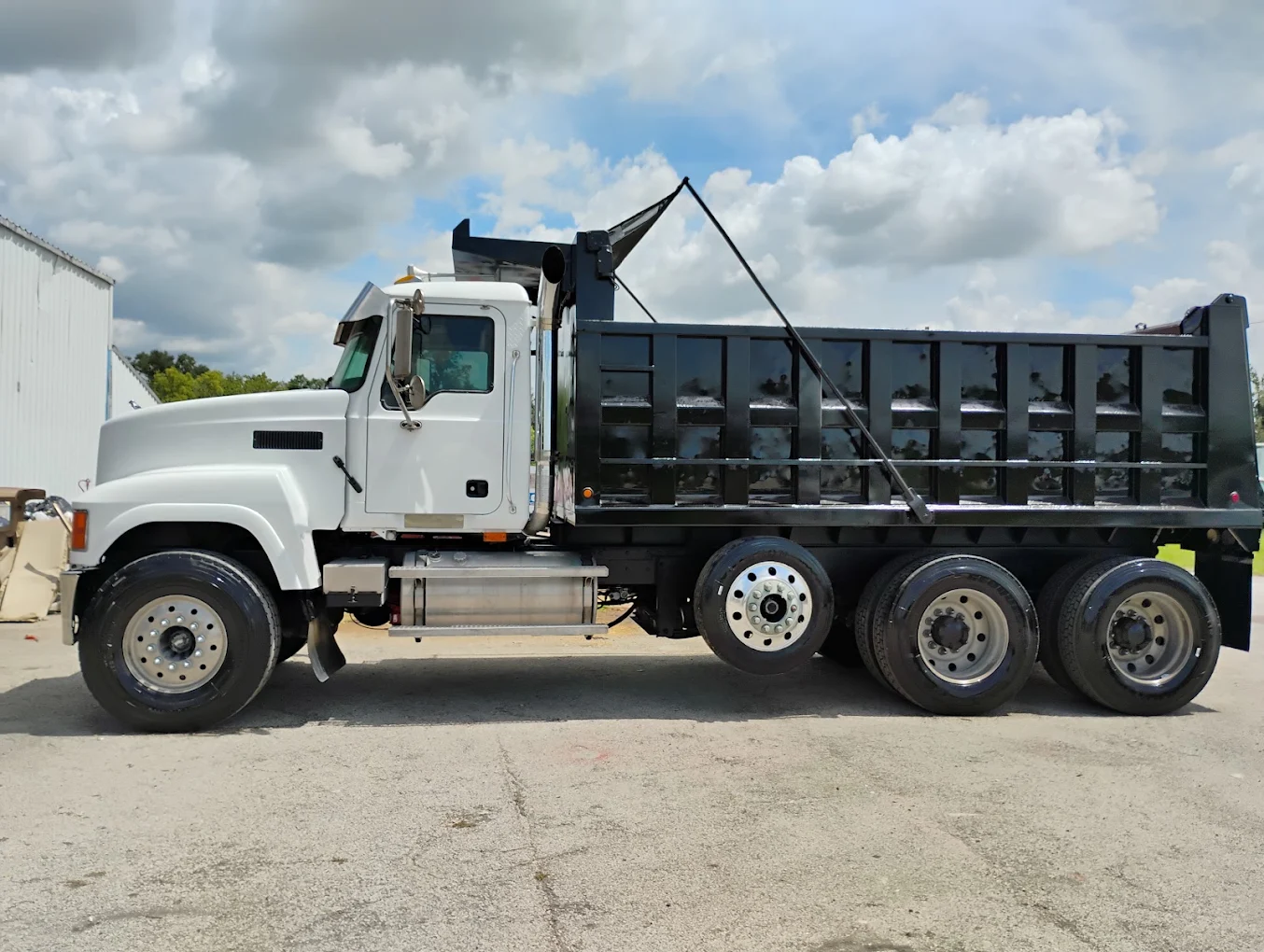 White and black dump truck with open bed parked on gravel lot