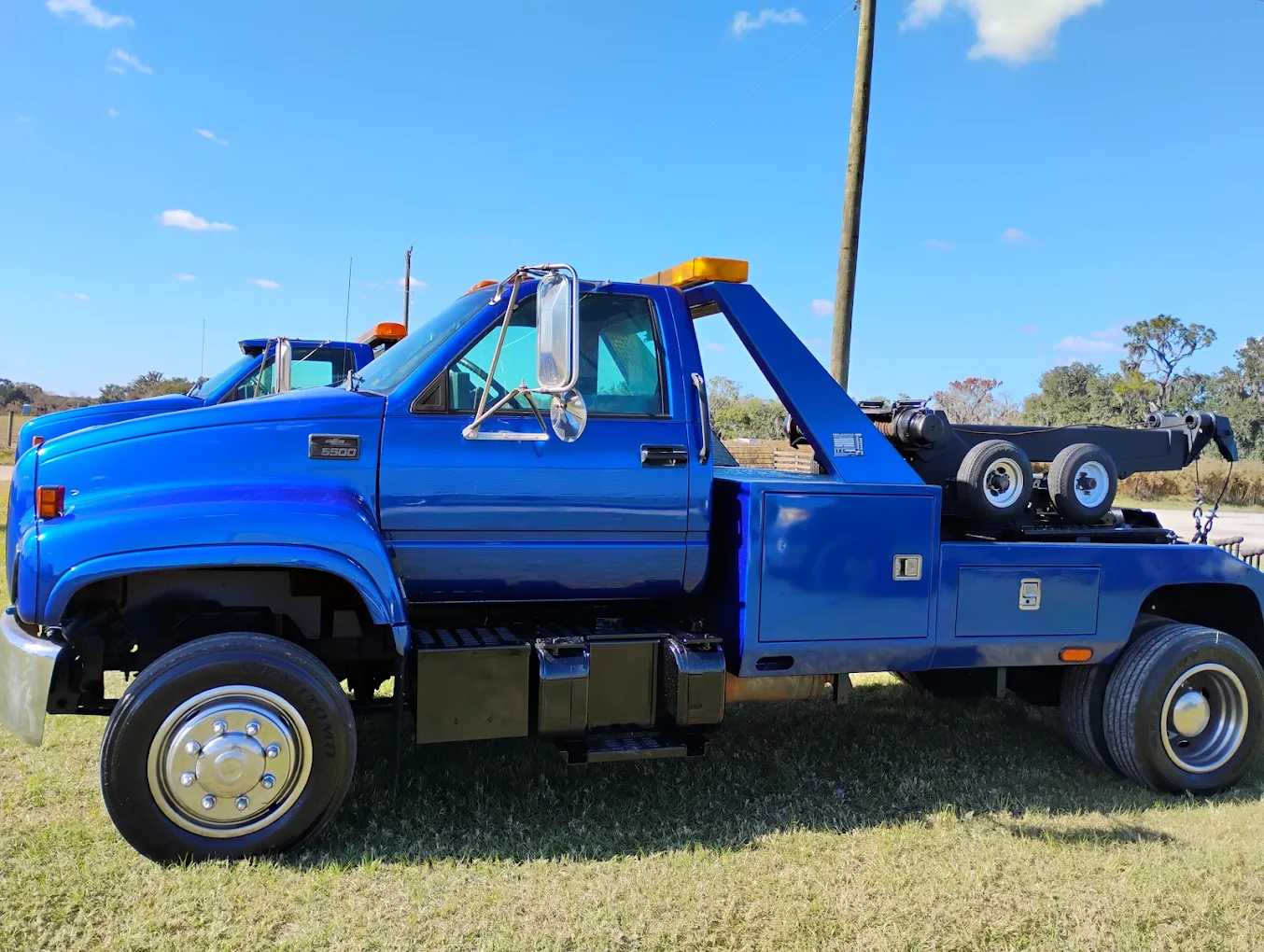 Blue GMC 5500 tow truck with wrecker boom and yellow lights parked outdoors