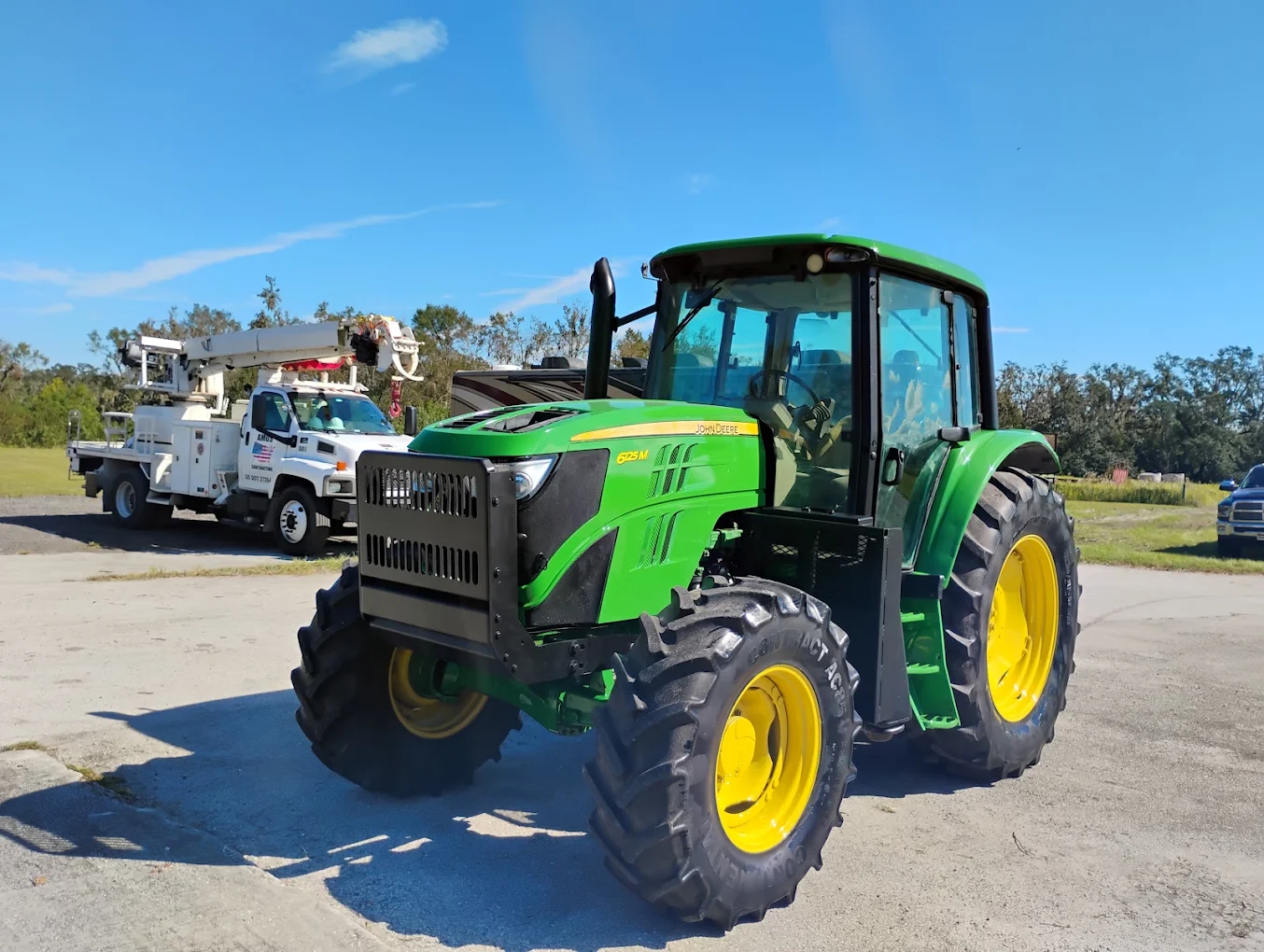 Bright green John Deere tractor with yellow wheels parked beside utility truck in outdoor lot