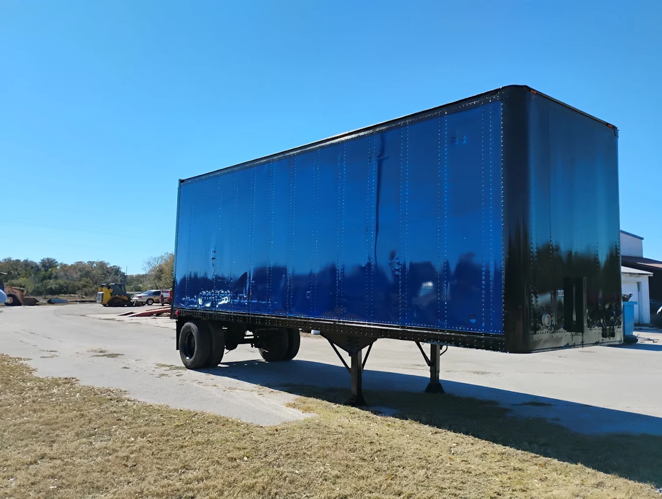 Blue commercial semi-trailer parked at an industrial yard with clear sky