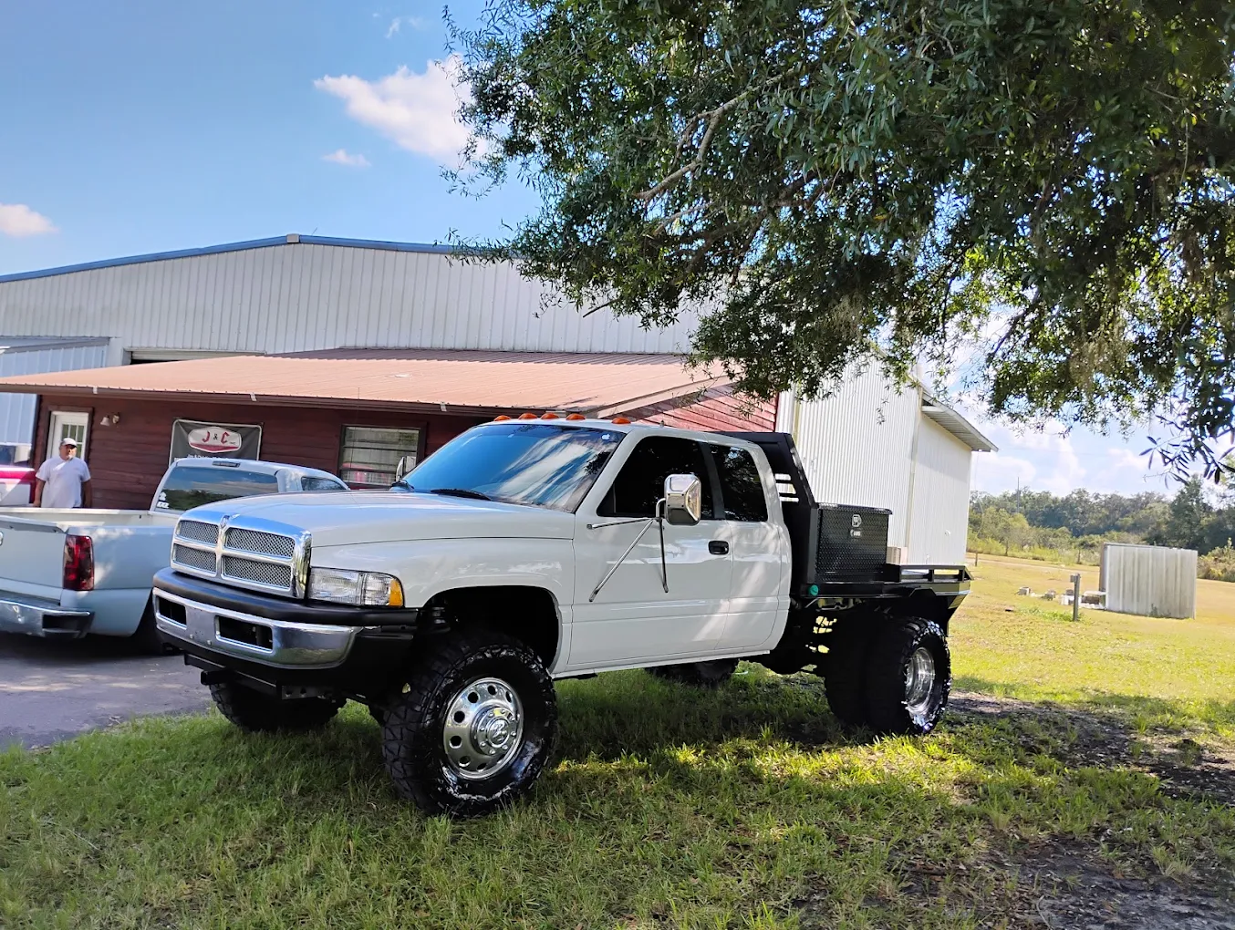 White lifted Dodge Ram pickup truck with custom black bed parked at rural auto shop