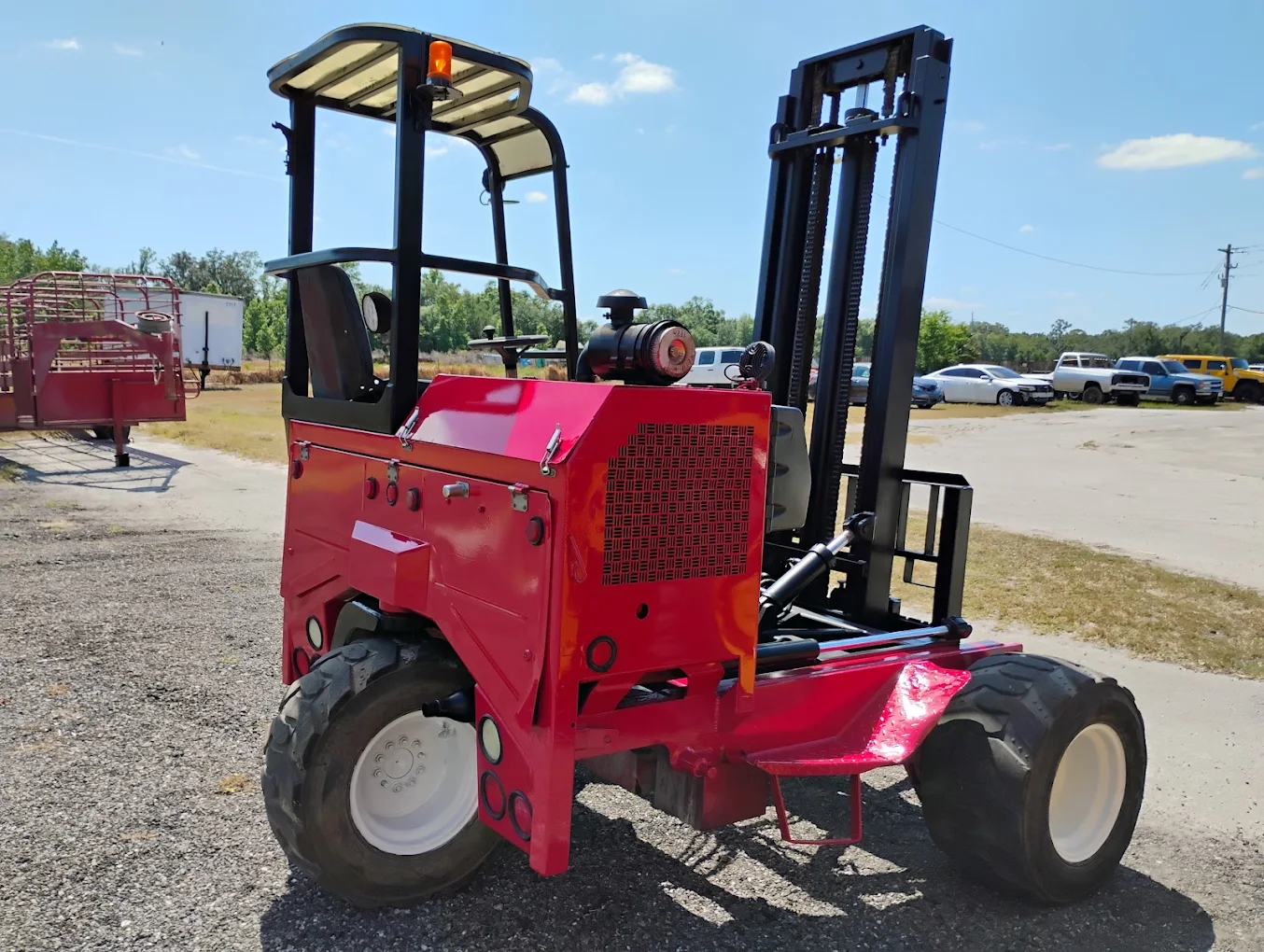 Red industrial forklift with black mast and forks on gravel lot