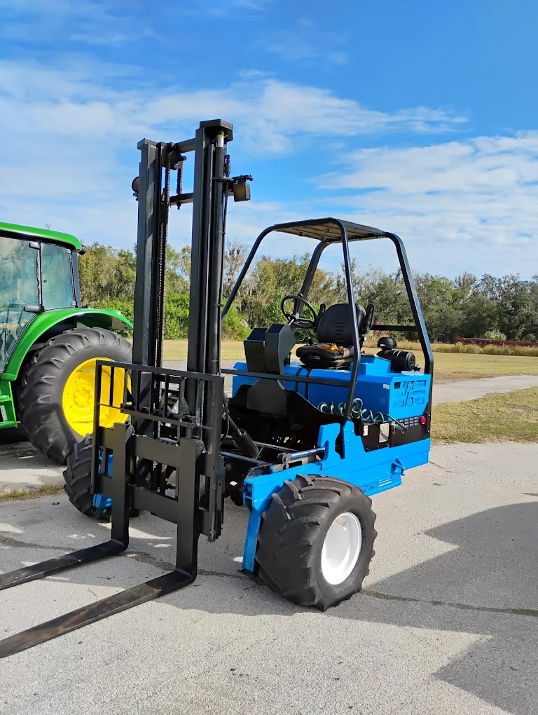 Blue rough terrain forklift with black mast and tires on asphalt lot