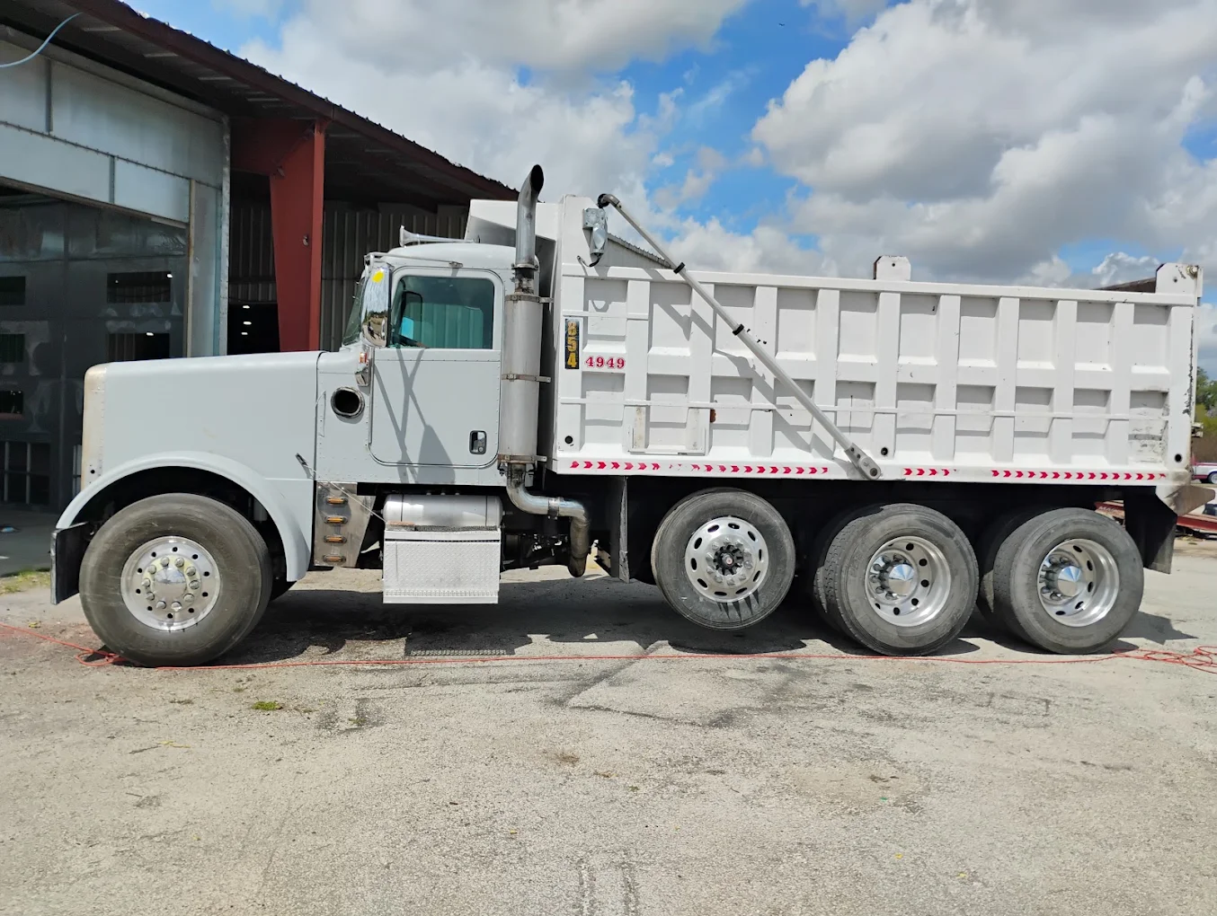 White dump truck with red striped bed parked outside industrial warehouse