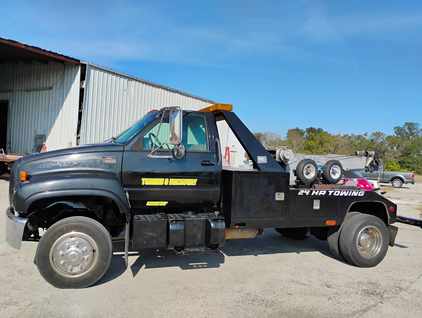 Black tow truck with yellow and pink accents parked at industrial facility