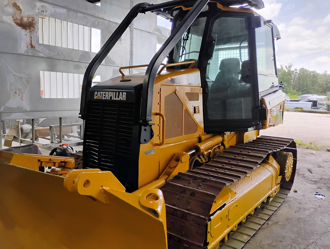 Yellow Caterpillar compact tracked loader with open cab door parked outside industrial building