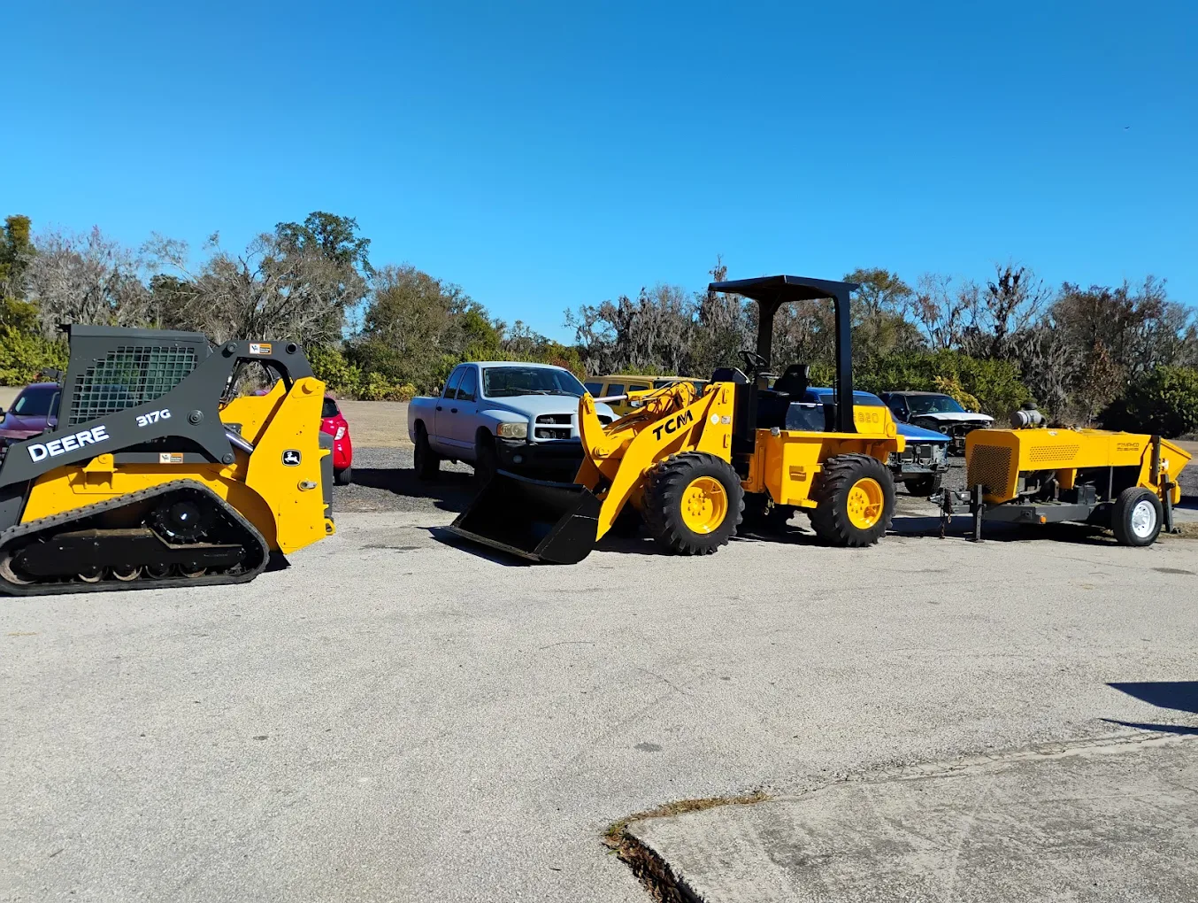 Yellow construction equipment including skid steer loader, wheel loader, and vintage machinery displayed at outdoor lot