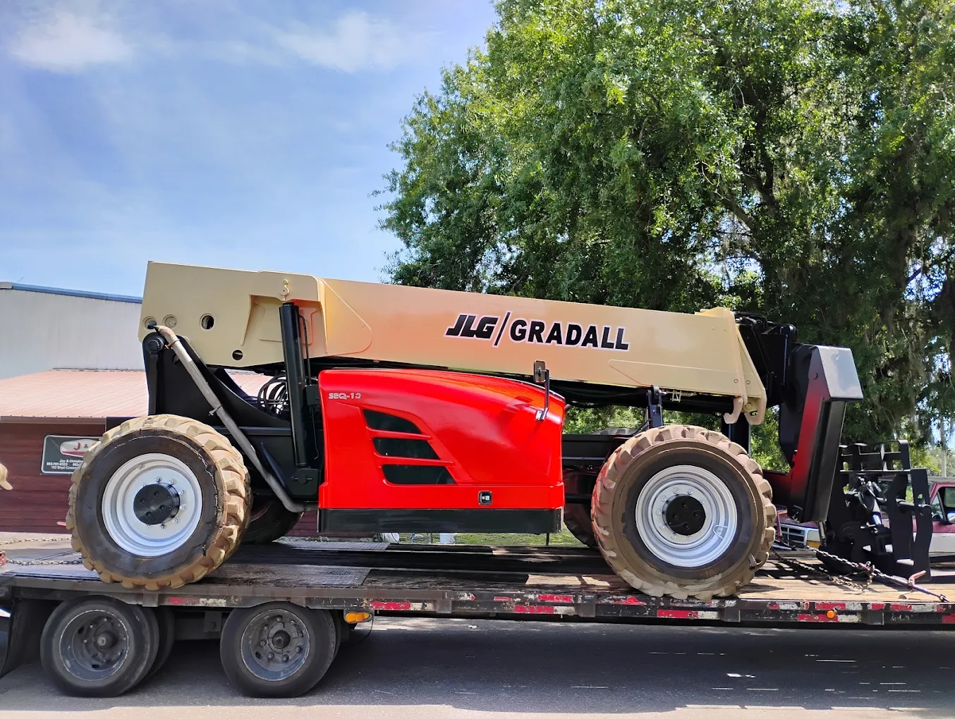 JLG Gradall telehandler with red cab on transport trailer under trees
