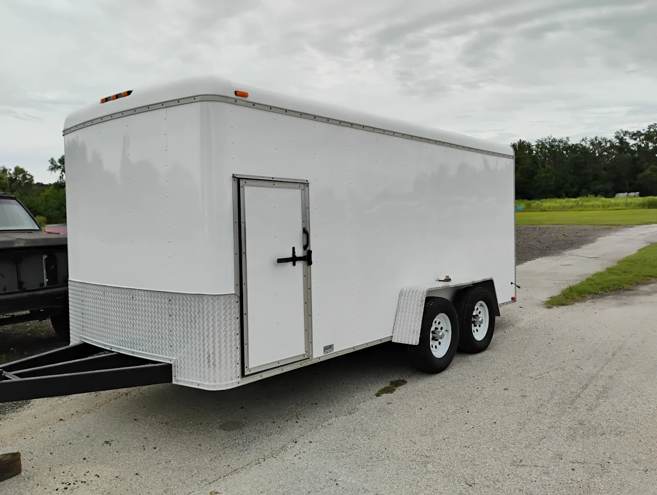 White enclosed cargo trailer with dual axles parked on gravel lot