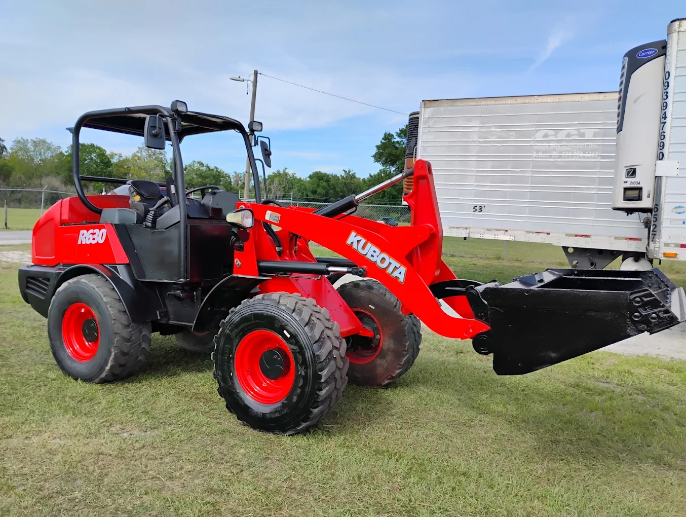 Red Kubota R630 compact tractor with front loader and blade attachment displayed at outdoor dealership