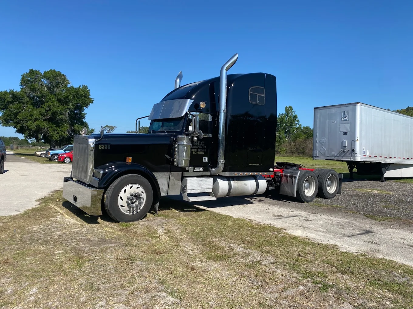 Black semi truck with chrome stacks and sleeper cab attached to white refrigerated trailer in lot