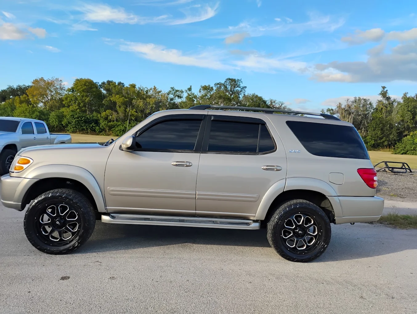 Silver Toyota Sequoia SUV with custom wheels parked on asphalt lot with trees in background