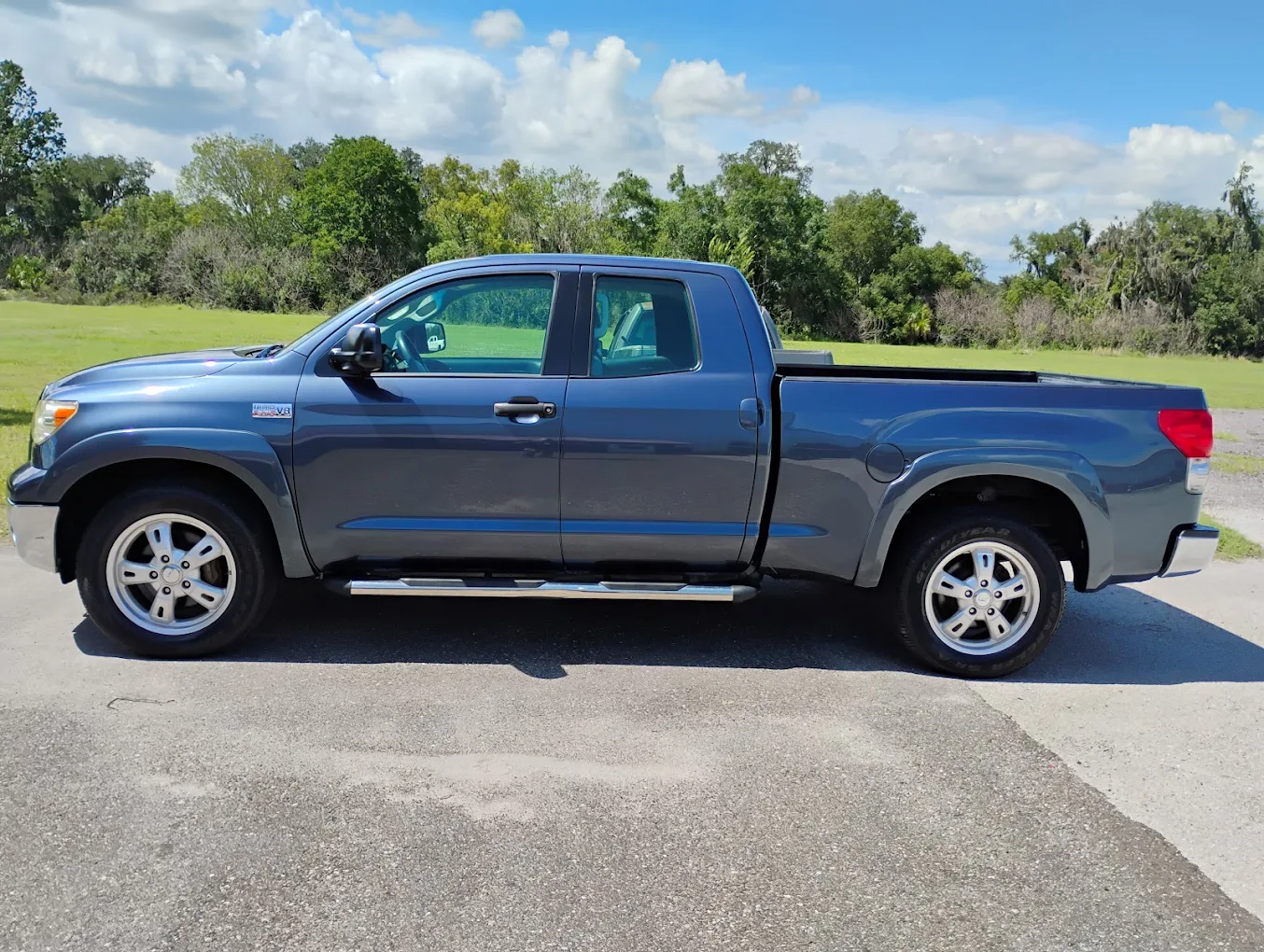 Blue Toyota Tundra pickup truck parked on driveway with trees and grass in background