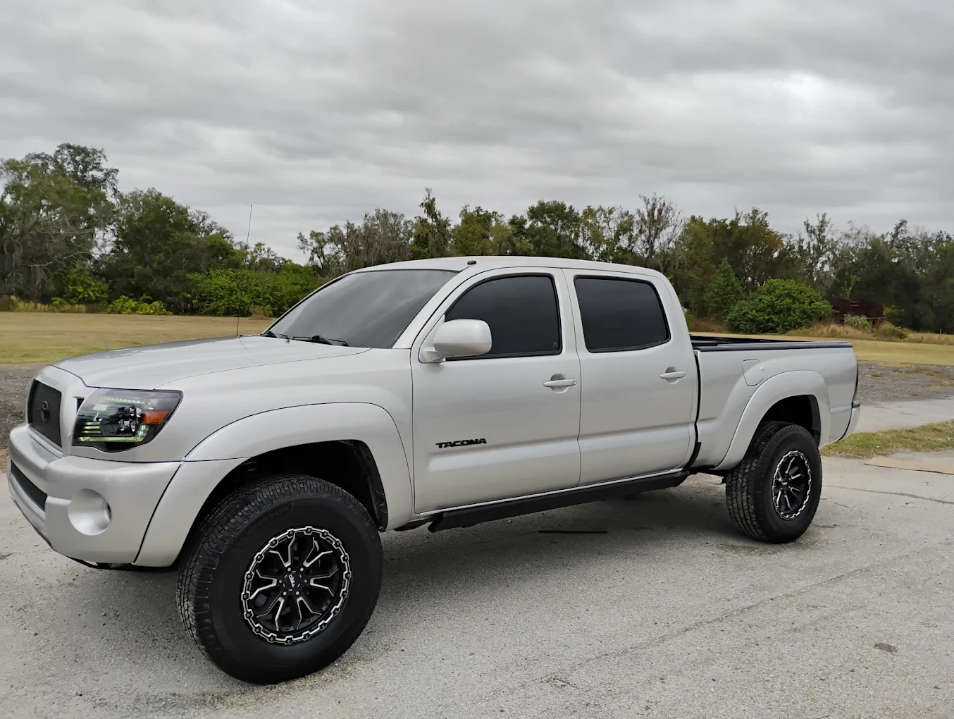 White Toyota Tacoma pickup truck with custom wheels parked on asphalt