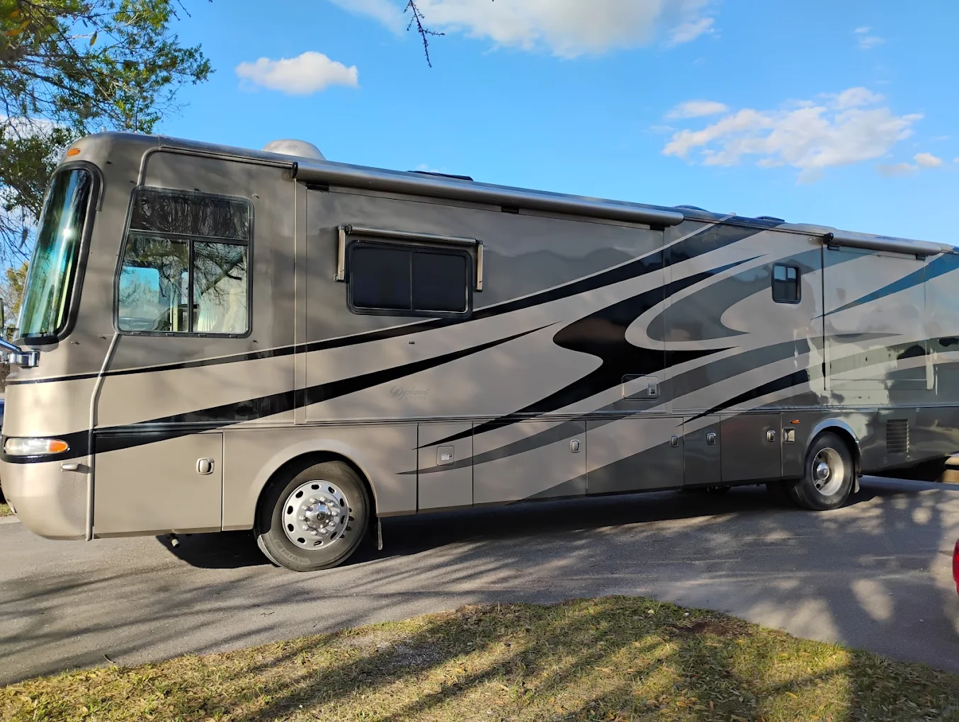 Beige and black motorhome with curved graphics parked on asphalt lot under blue sky