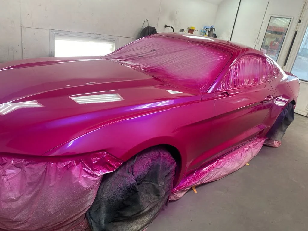 Bright magenta car covered in protective plastic wrap in indoor paint booth