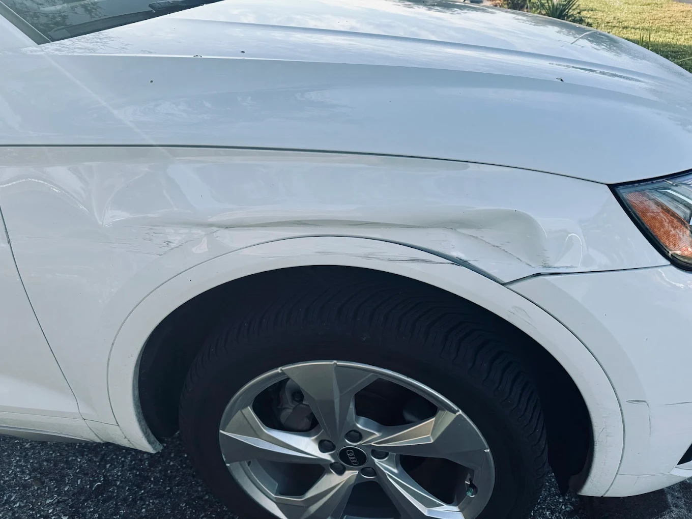 White vehicle hood and fender with dent damage next to wheel