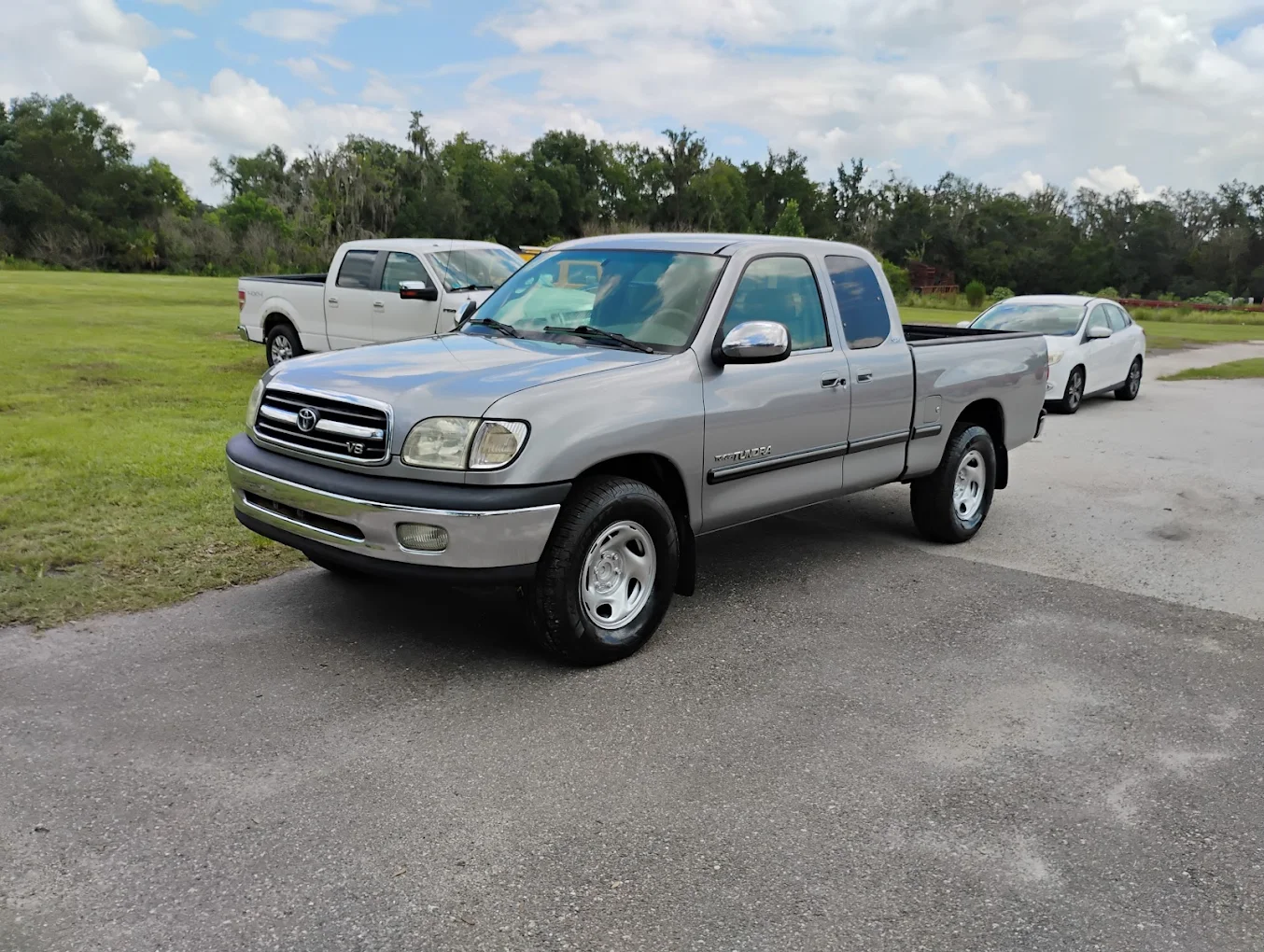 Silver Toyota Tundra pickup truck parked on asphalt with other vehicles and trees in background
