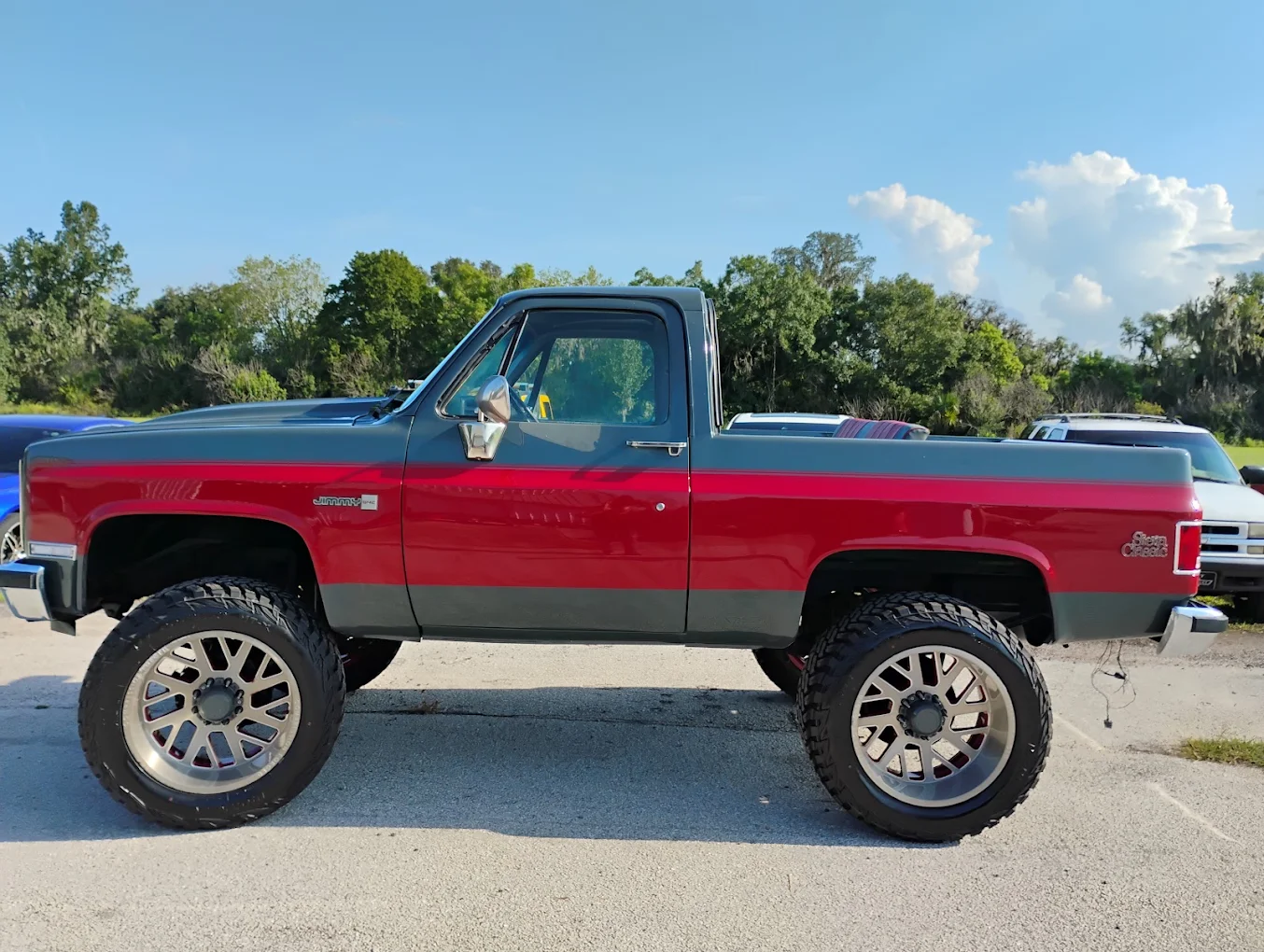 Red and gray lifted Chevrolet pickup truck with large wheels parked outdoors