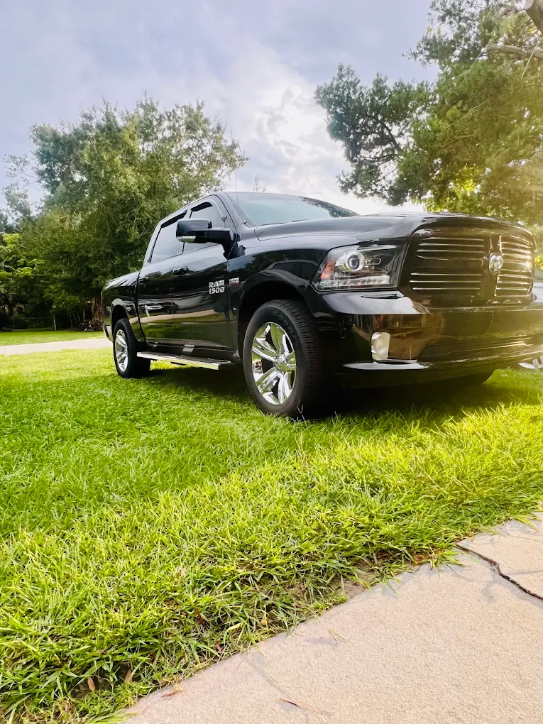 Black Ram pickup truck parked on grass with trees in background