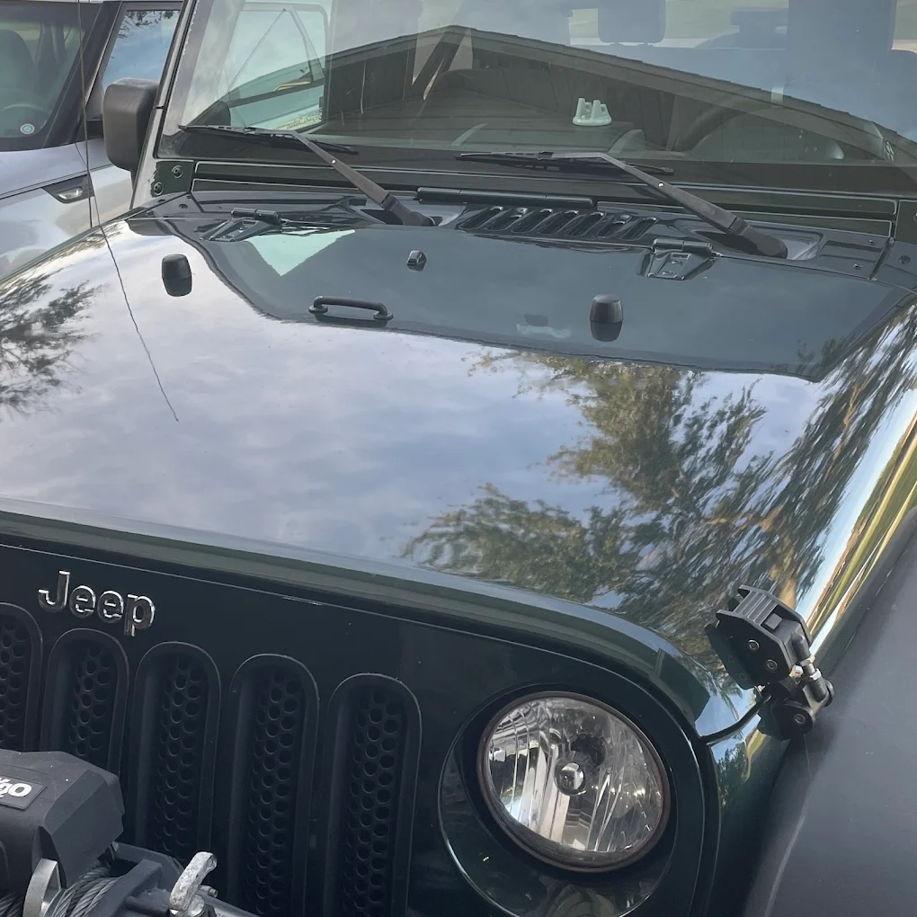 Open hood of black Jeep showing engine compartment and windshield reflection