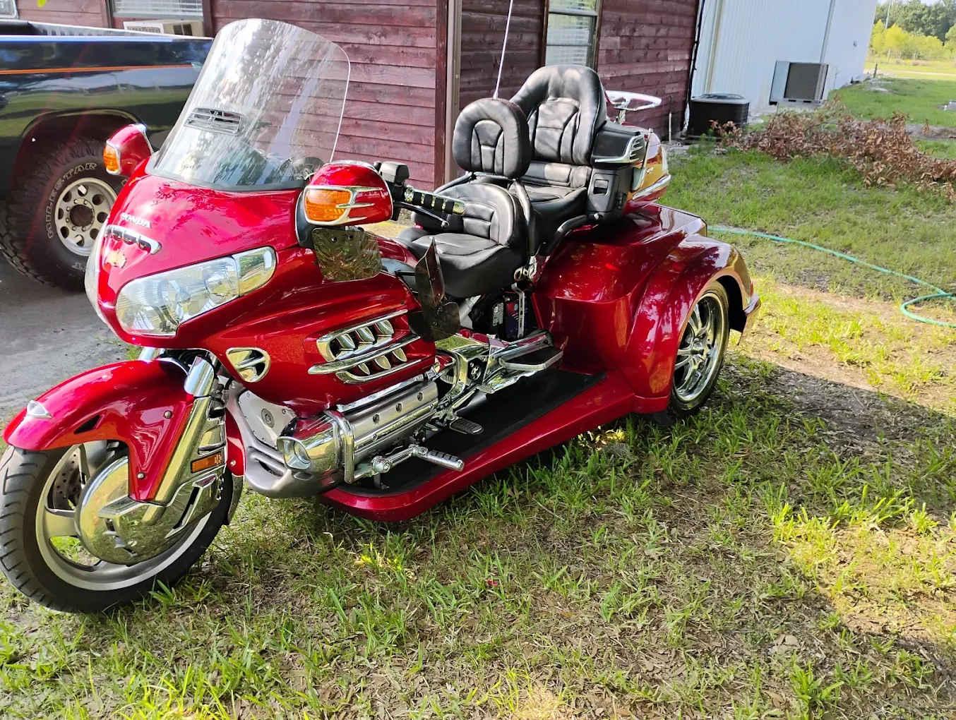 Red touring motorcycle with sidecar and windshield parked on grass near buildings